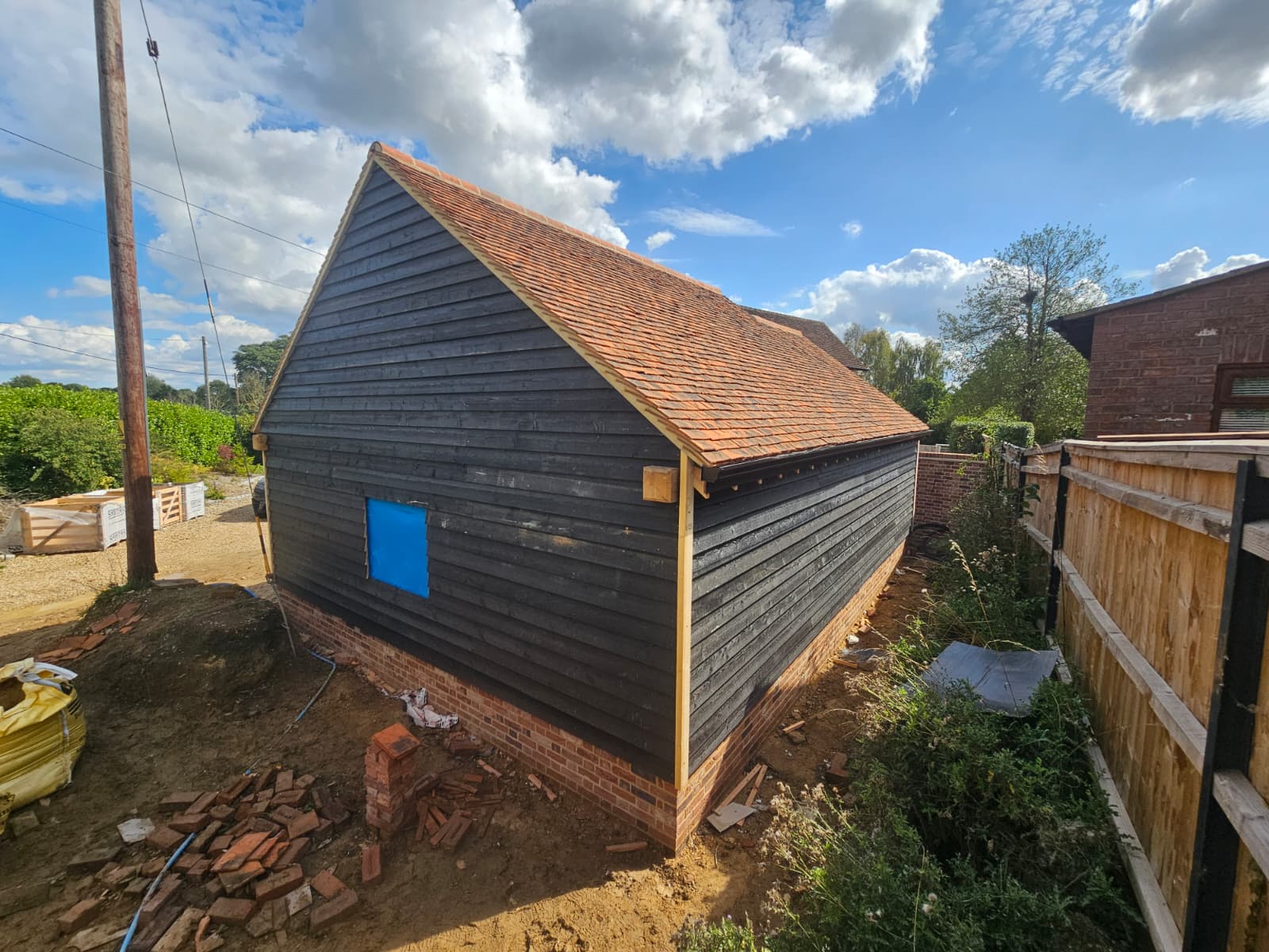 Finished oak-framed building in black feather-edge boarding with a clay tile roof
