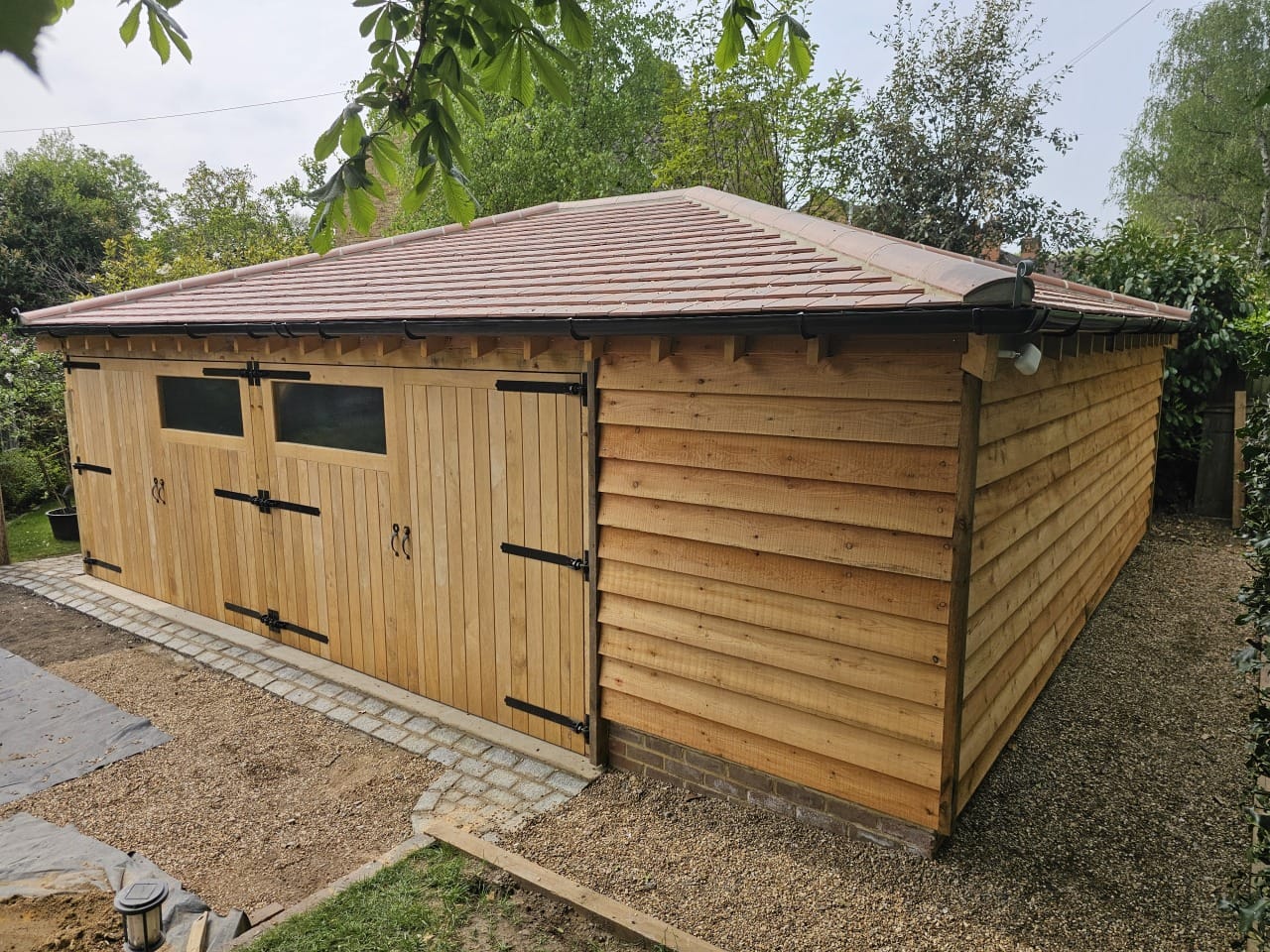 Completed oak frame garage with shiplap cladding, clay tile roof, and garage doors