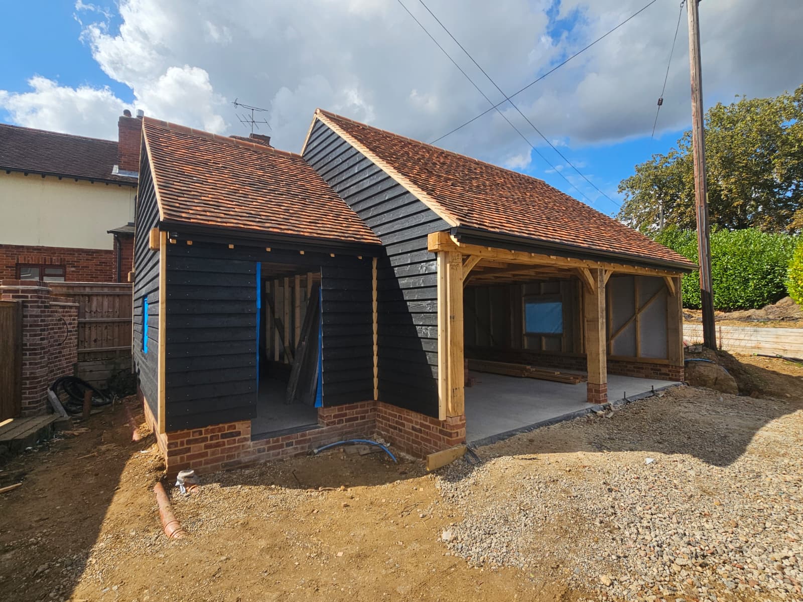 Completed oak frame barn with brick plinth, dark cladding, and open bays