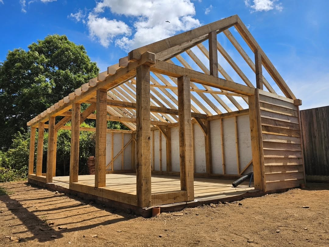 Bespoke oak frame raised on site, showing hand-cut posts and rafters against a blue sky