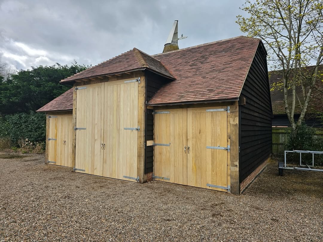 Completed three-bay oak-frame garage with hand-hung boarded doors and a clay-tile hipped roof